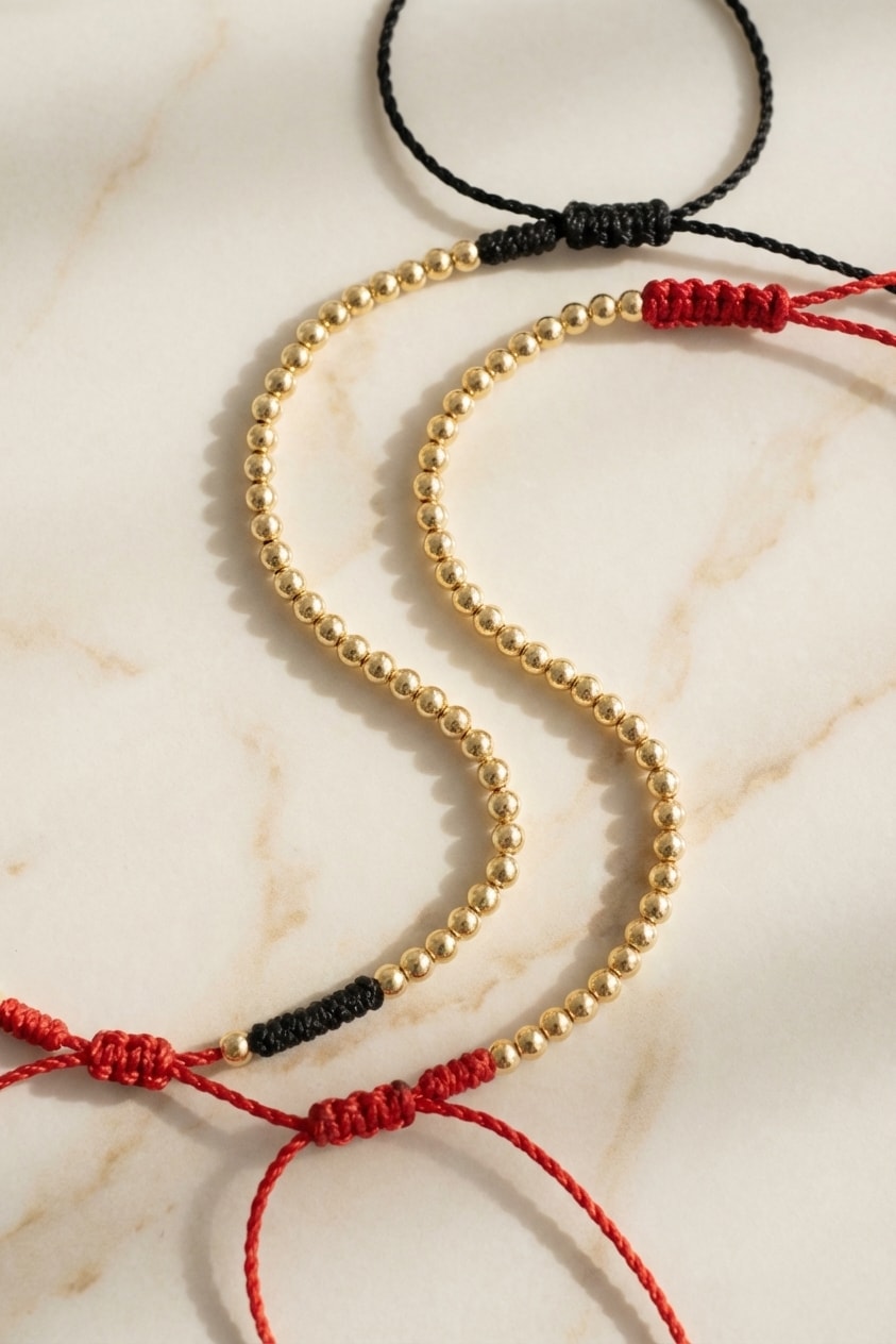 Pulsera Cordón Carmesí flat lay sobre mármol cremoso, composición elegante en oro laminado 18k NJL Jewelry