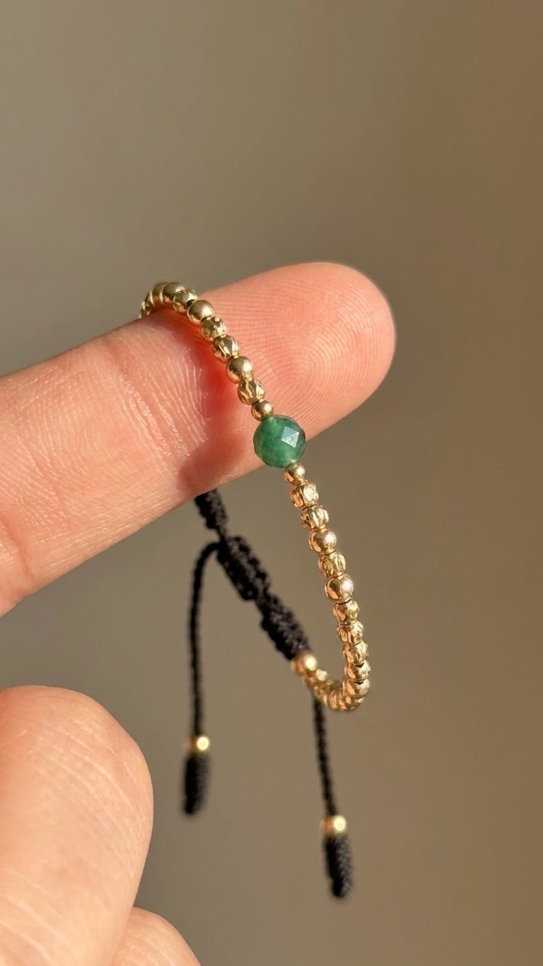 Pulsera fina con balines mini diamantados y esmeralda central oro laminado 18k detalle macro entre dedos, primer plano NJL Jewelry