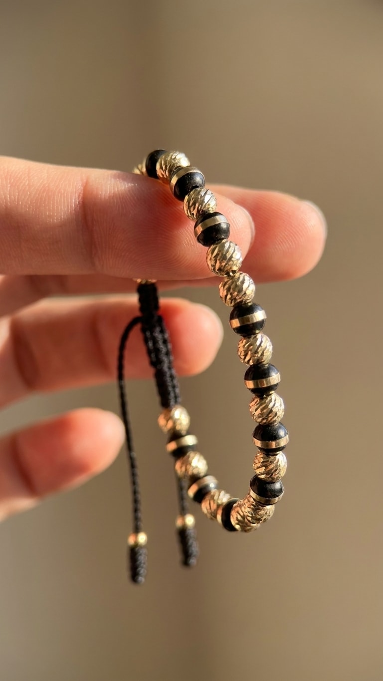 Pulsera macramé negro con balines diamantados oro laminado 18k detalle macro entre dedos, primer plano NJL Jewelry