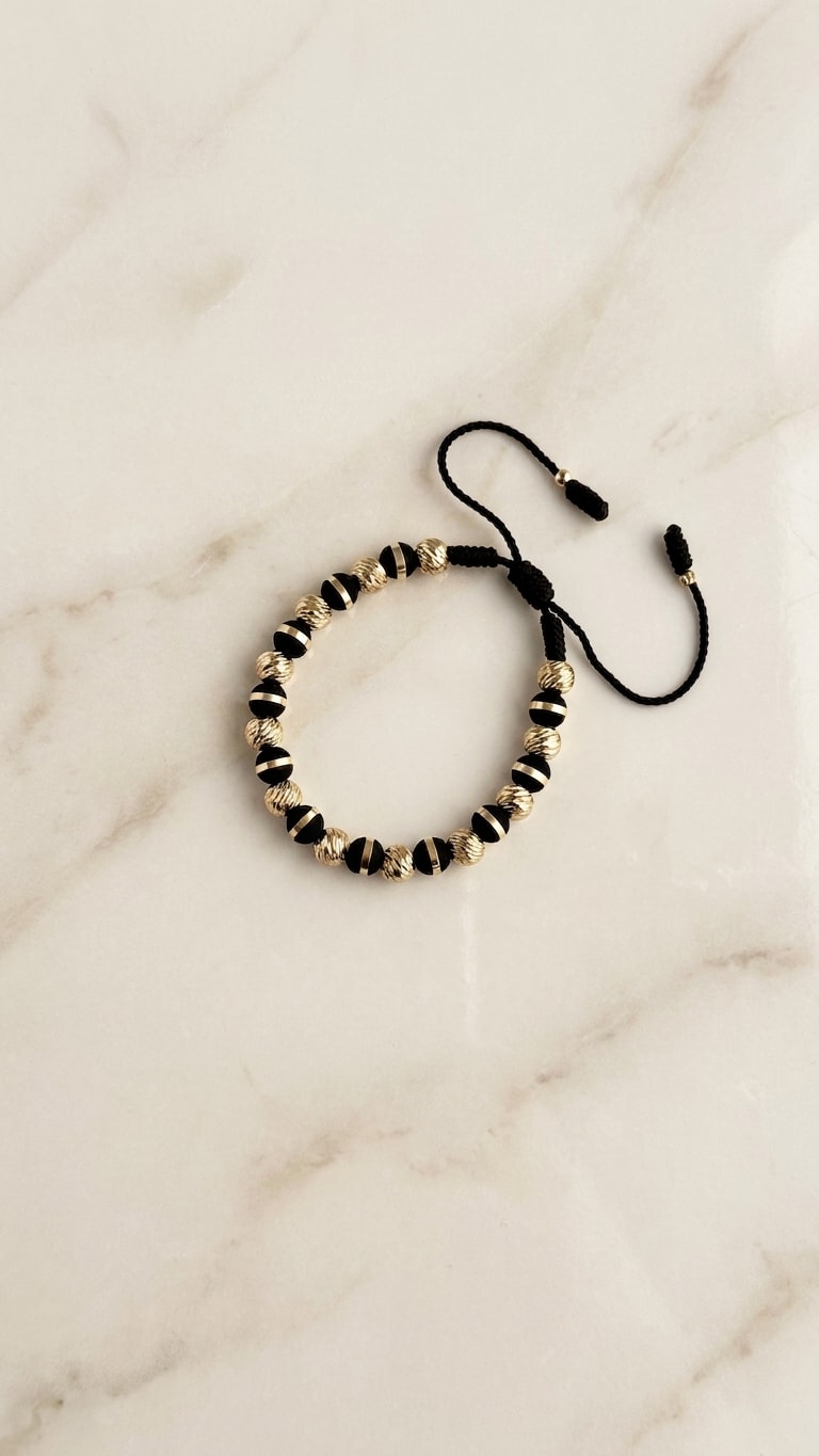 Pulsera macramé negro con balines diamantados oro laminado 18k flat lay sobre mármol cremoso, composición elegante NJL Jewelry