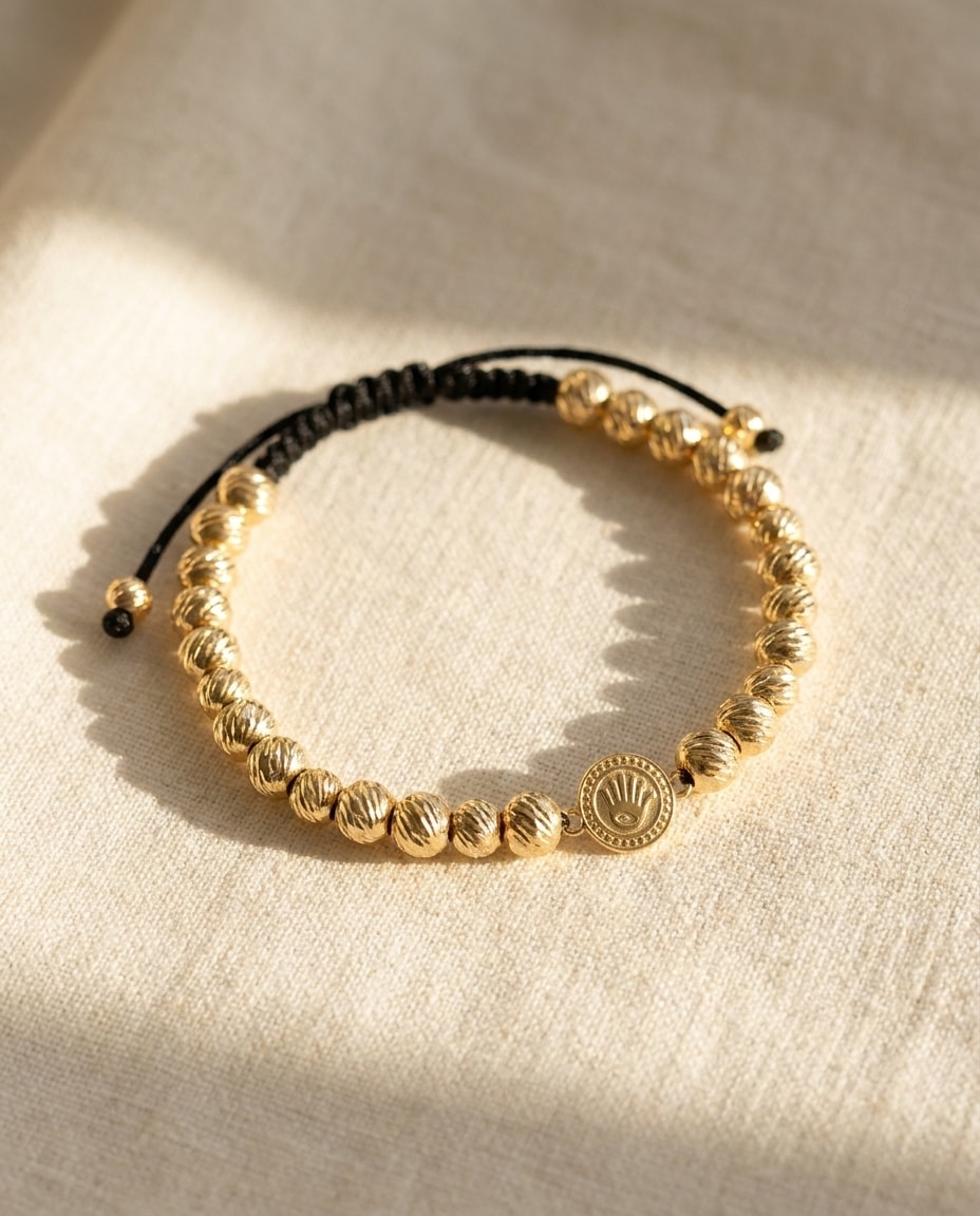 Pulsera balines diamantados con medalla central oro laminado 18k sobre lino crema, flat lay editorial NJL Jewelry