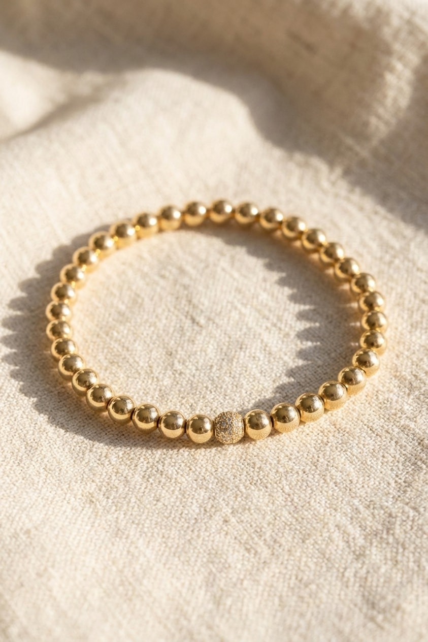 Pulsera Palo de Rosa con Bola Central sobre lino cremoso, flat lay editorial en oro laminado 18k NJL Jewelry