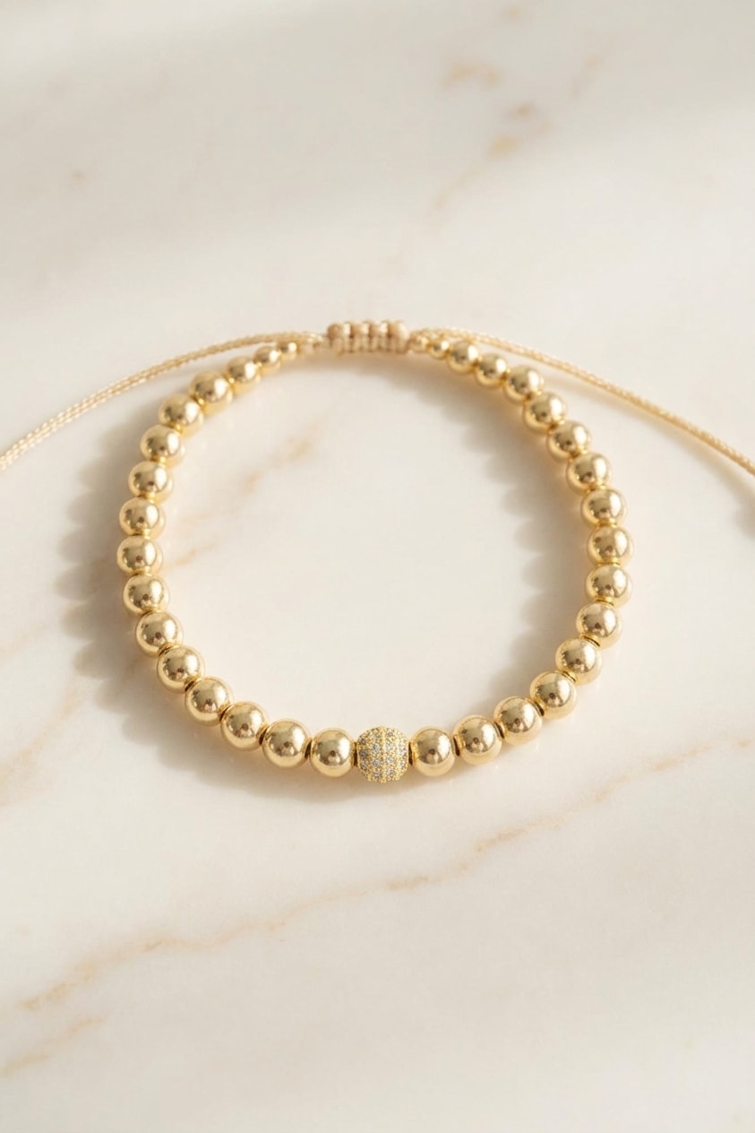 Pulsera Palo de Rosa con Bola Central flat lay sobre mármol cremoso, composición elegante en oro laminado 18k NJL Jewelry