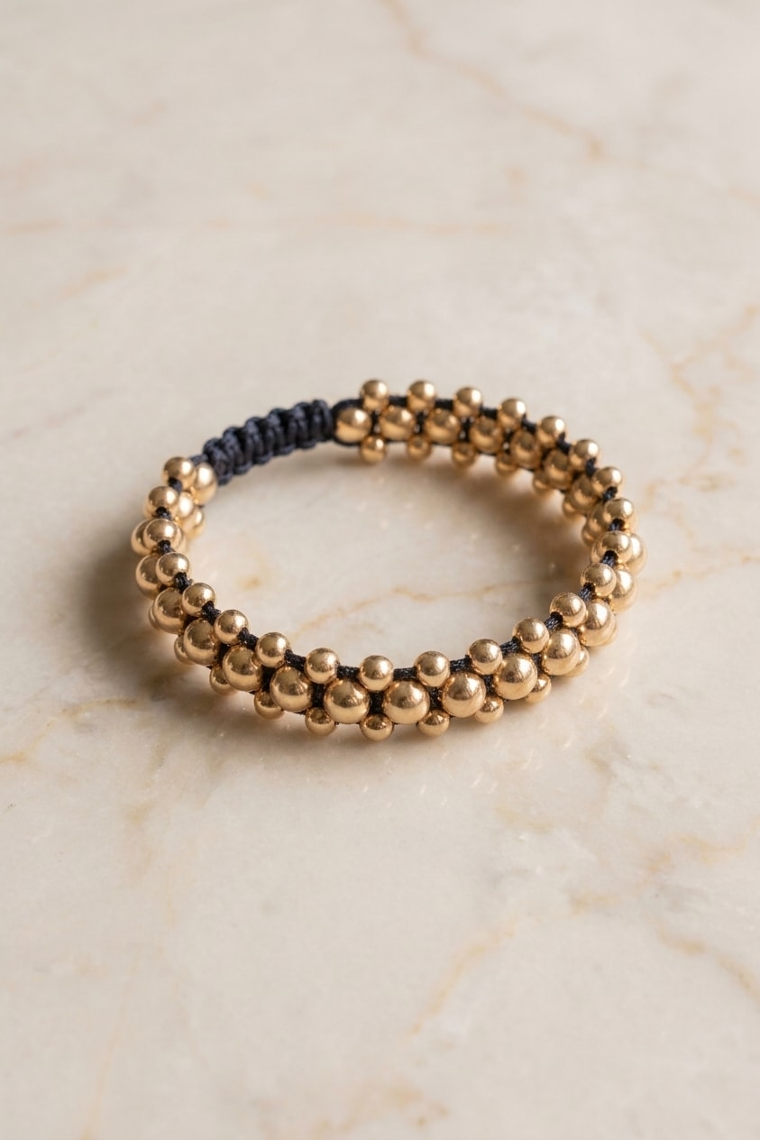 Pulsera triple carril liso de balines oro laminado 18k flat lay sobre mármol cremoso, composición elegante NJL Jewelry