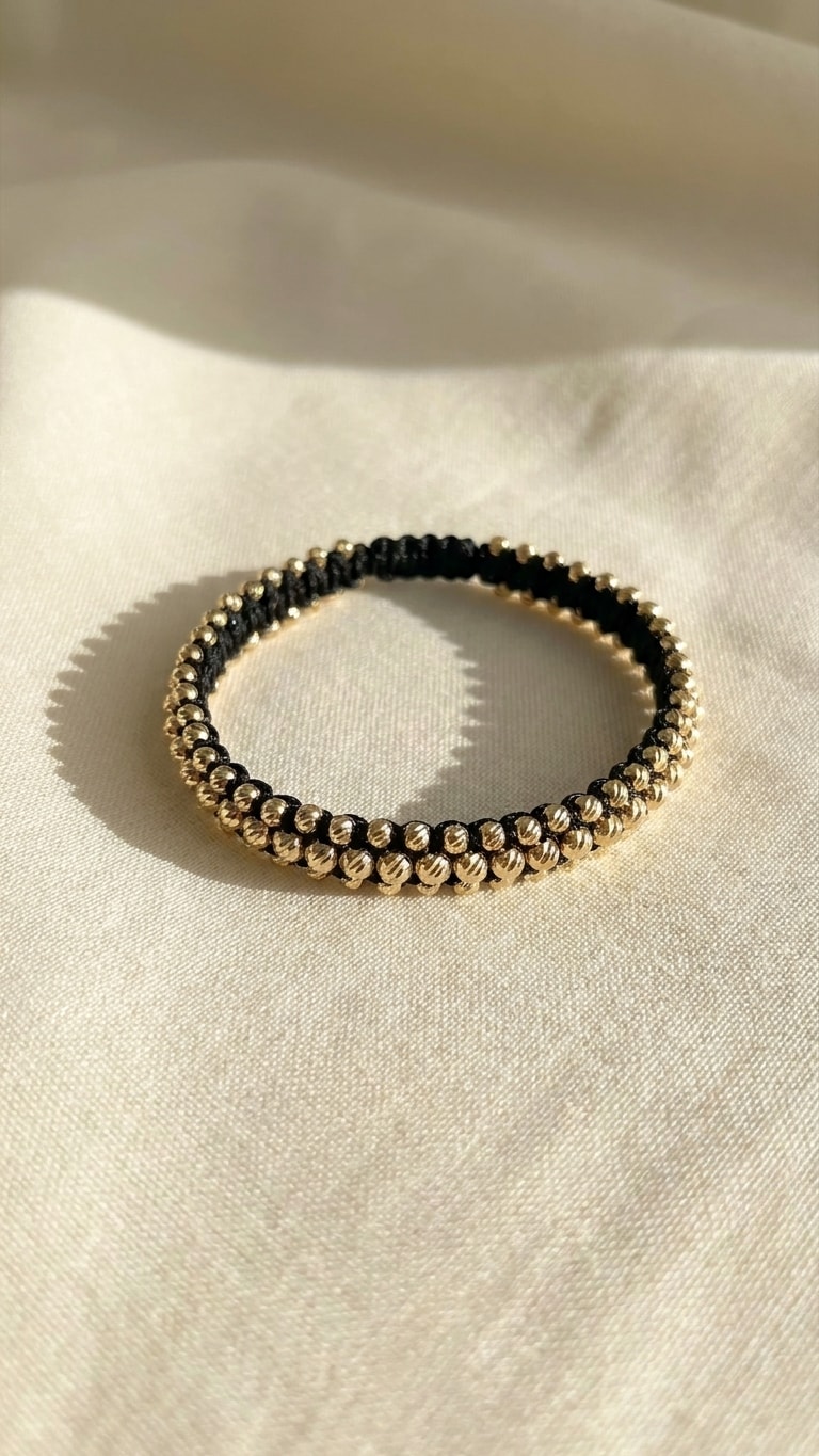 Pulsera triple carril macramé negro con balines diamantados gruesos oro laminado 18k sobre lino crema, flat lay editorial NJL Jewelry