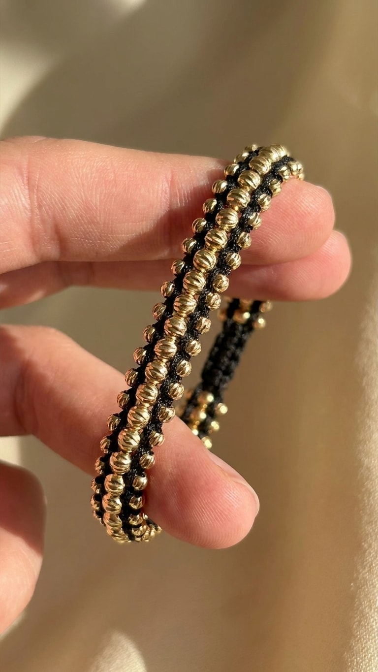 Pulsera triple carril macramé negro con balines diamantados gruesos oro laminado 18k detalle macro entre dedos, primer plano NJL Jewelry
