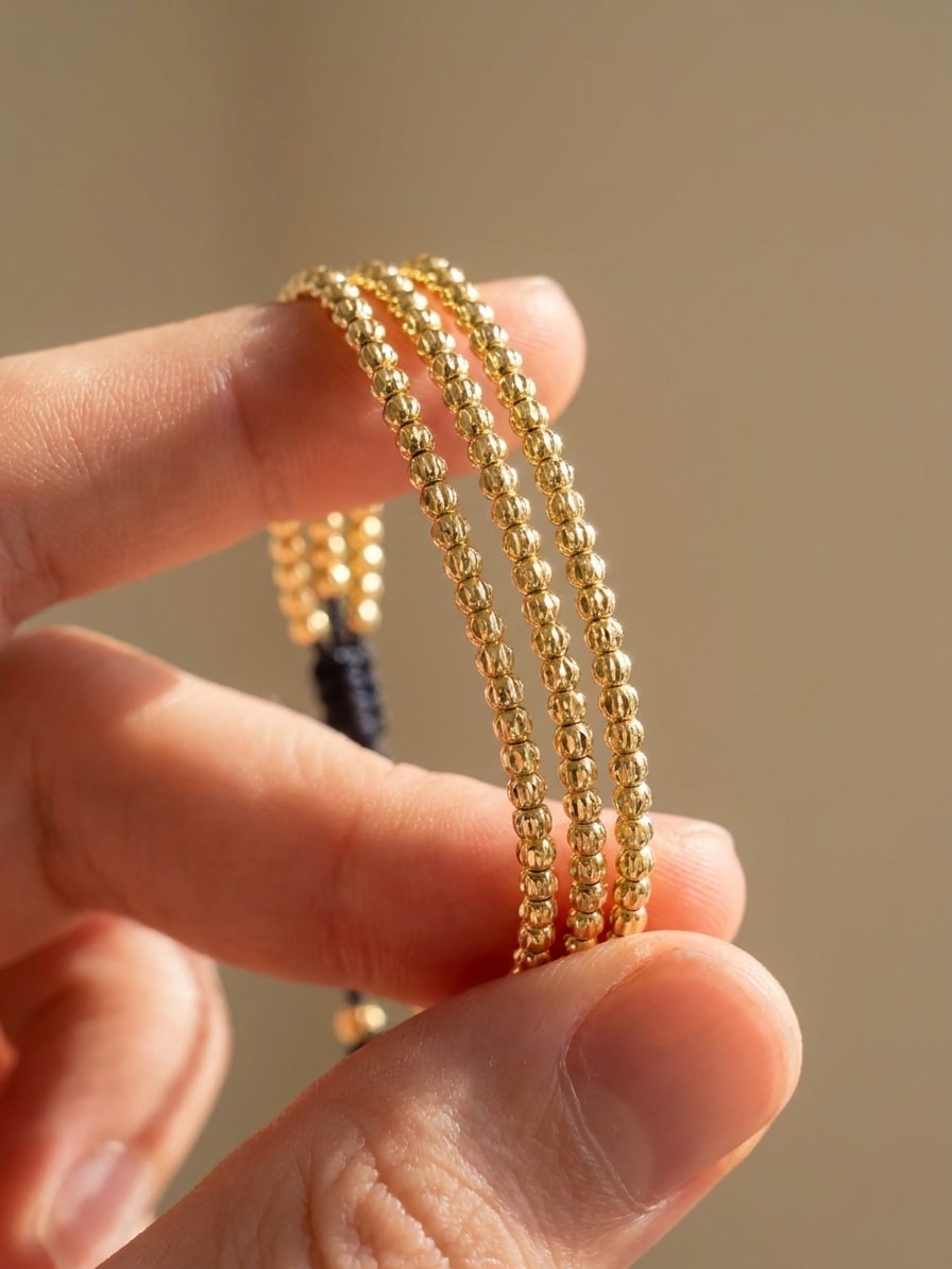 Set de 3 pulseras finas con balines mini diamantados oro laminado 18k detalle macro entre dedos, primer plano NJL Jewelry